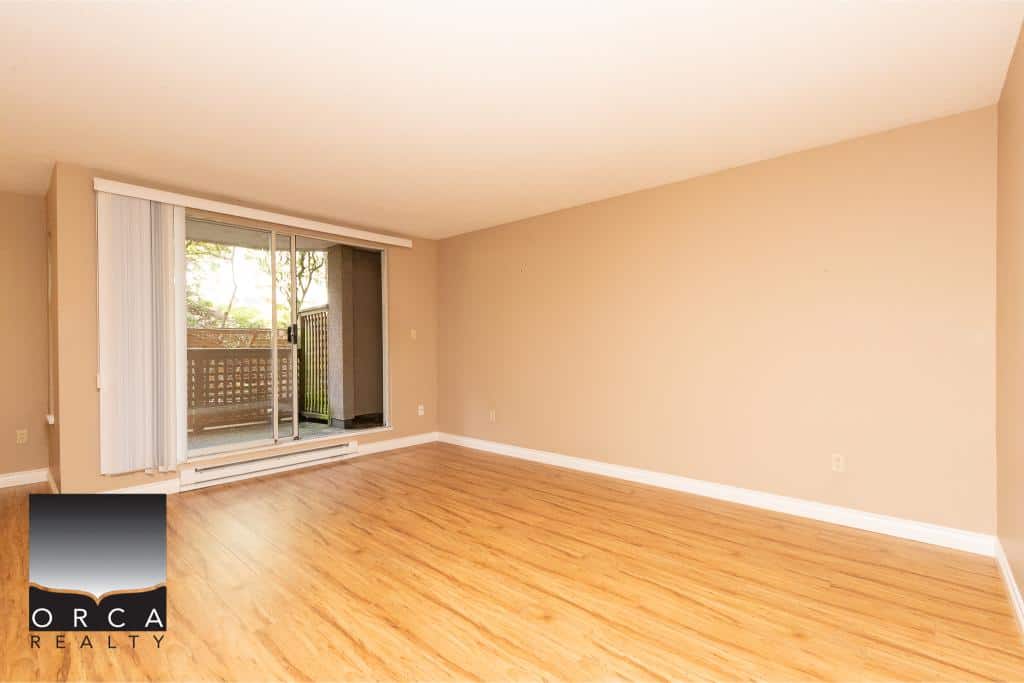Spacious empty living room with large sliding glass doors leading to a balcony, hardwood flooring, neutral beige walls, ideal for Vancouver real estate buyers.