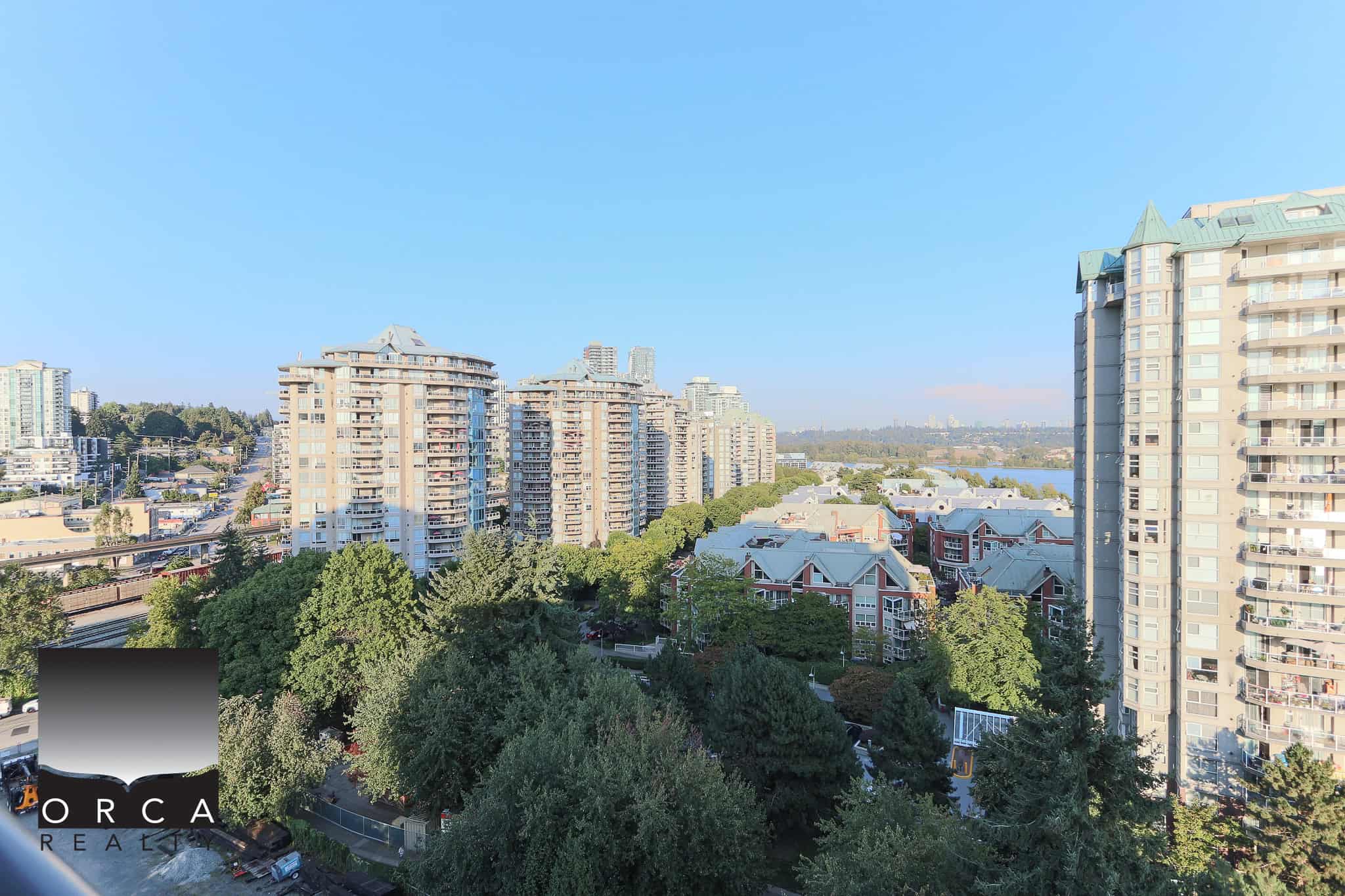 Stunning cityscape view from Orca Realty Inc. showcasing modern high-rise condominiums, lush green trees, and scenic river in the background, perfect for Vancouver real estate investments.