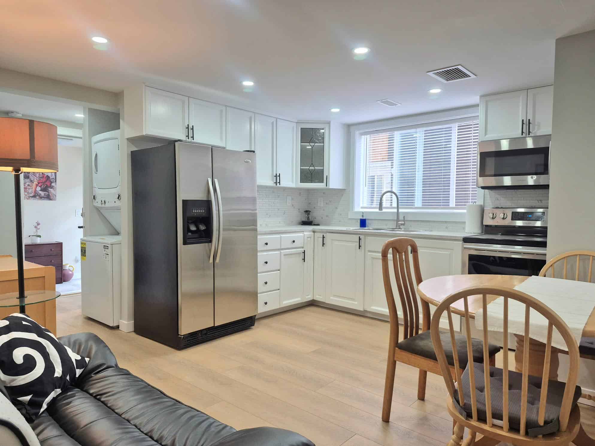 Modern kitchen and dining area with white cabinets, stainless steel appliances, and hardwood floors, featuring ample natural light from large windows; ideal for Vancouver Island real estate.