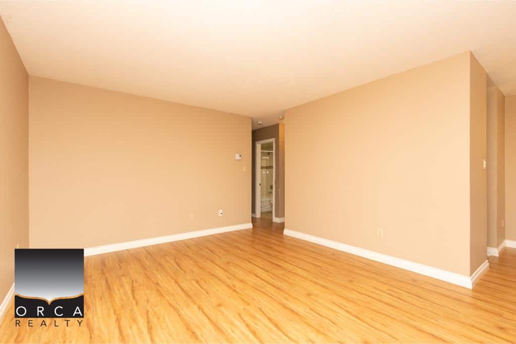 Spacious empty living room with hardwood floors and beige walls, ideal for home staging or future buyers.