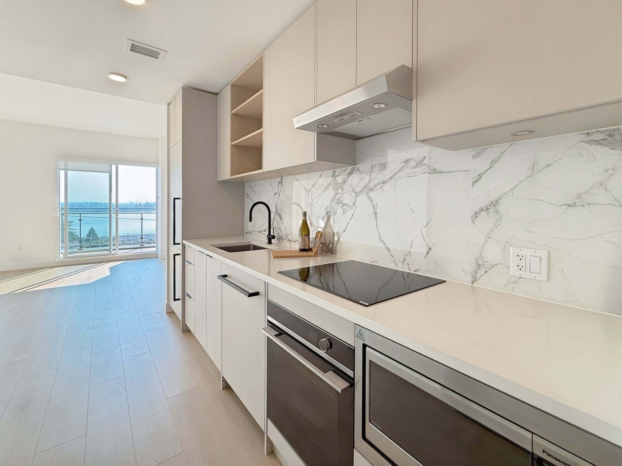 IMG_0395 Sleek modern kitchen with white cabinetry, marble backsplash, and black appliances in a high-rise condo overlooking water views in Vancouver, BC. Perfect for contemporary urban living.