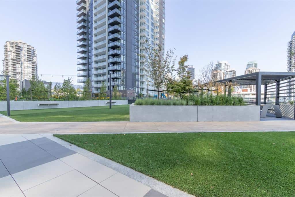 Modern urban park with lush green landscaping and high-rise residential buildings in the background, ideal for outdoor relaxation and community gatherings in Vancouver.