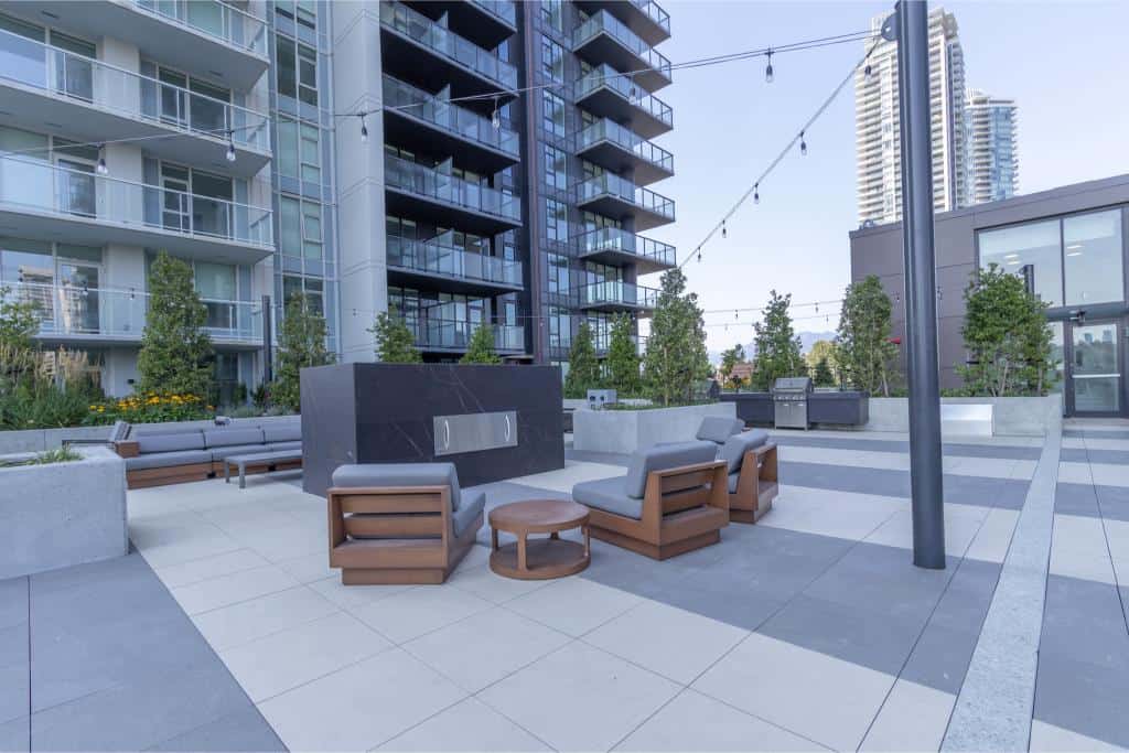 Modern outdoor rooftop patio in downtown Vancouver with stylish seating areas, string lights, lush greenery, and city skyline views, ideal for urban living and real estate in BC.