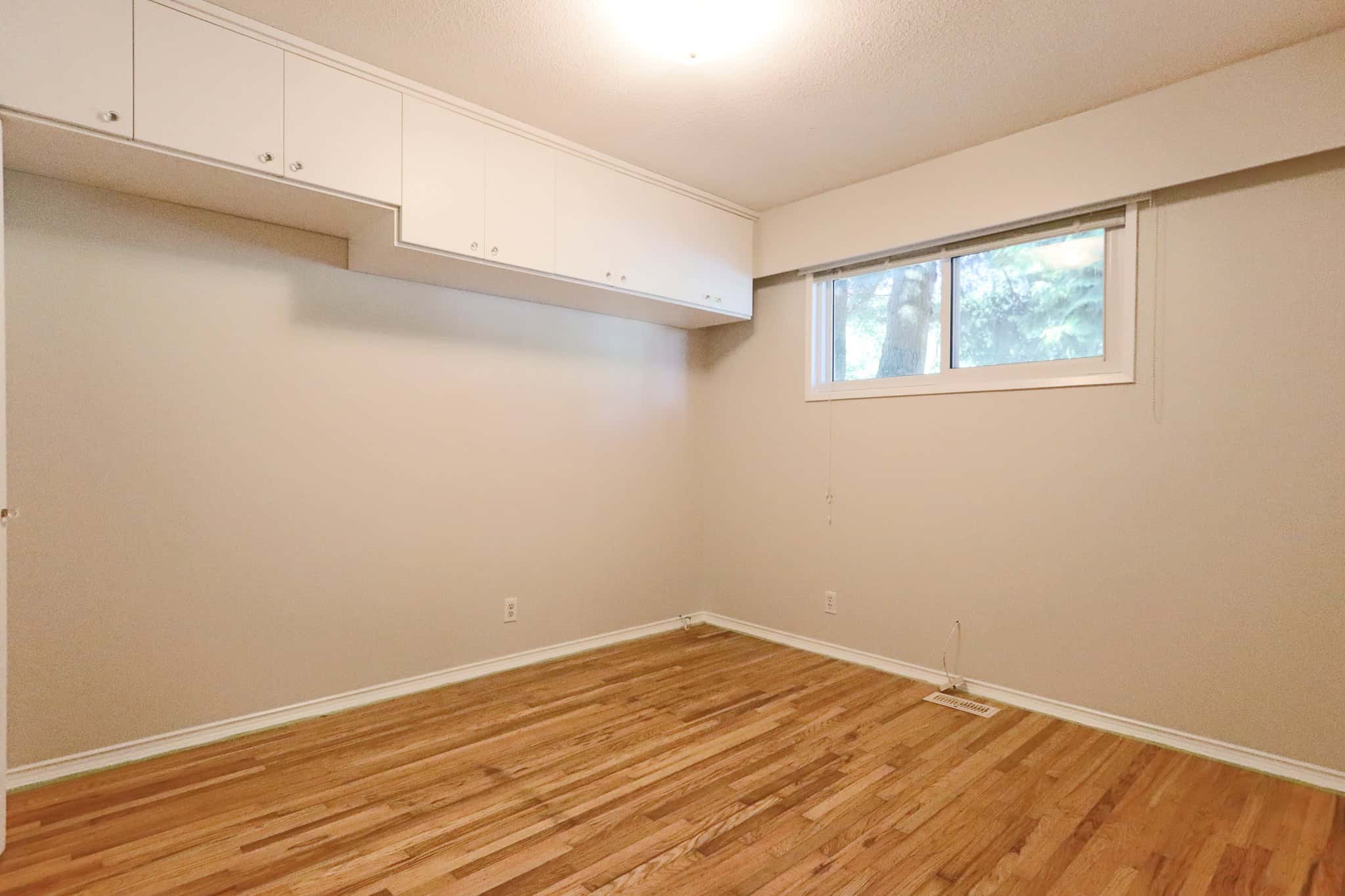 Bright empty room with hardwood floors, white walls, a large window, and built-in white cabinets, ideal for Vancouver and Victoria area home staging or real estate listings.