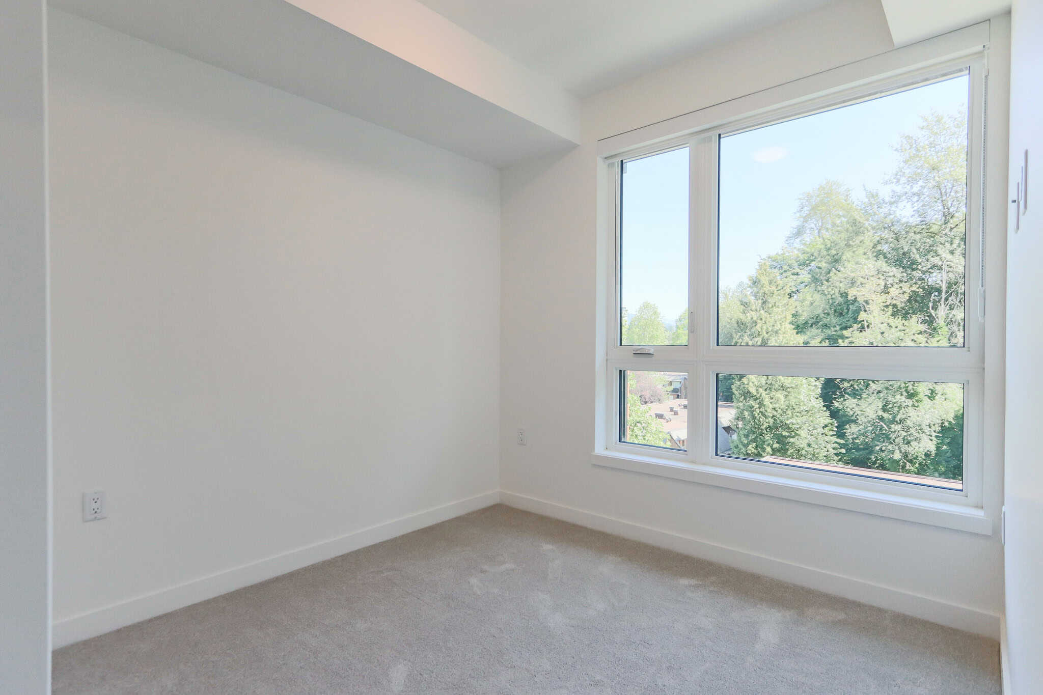 Bright, modern bedroom with large windows offering natural light and scenic views, featuring clean white walls and neutral carpet flooring, ideal for Vancouver Island real estate.