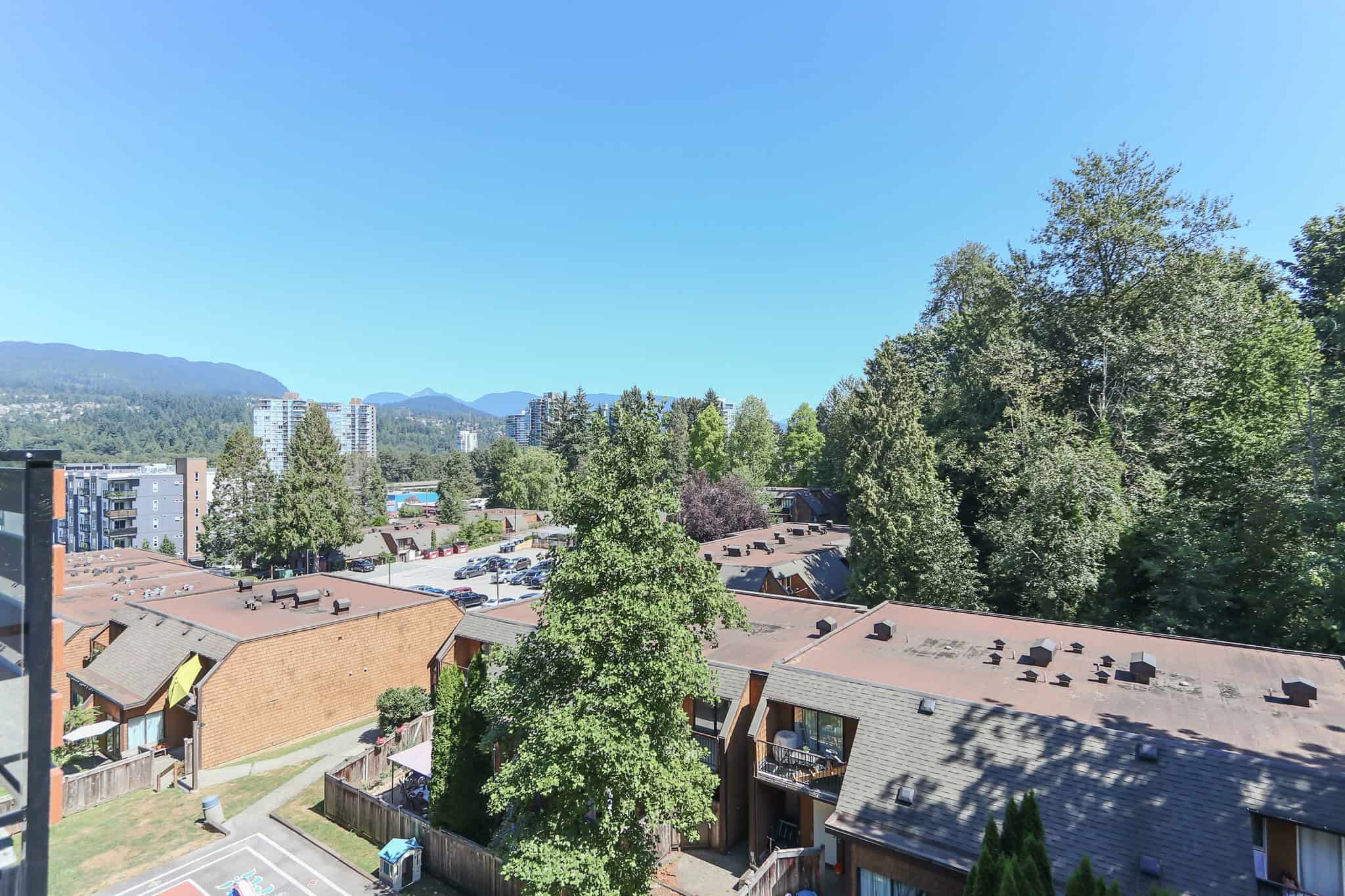 Breathtaking view of lush green trees and residential rooftops with mountains in the background, ideal for Vancouver real estate buyers seeking scenic surroundings and urban amenities.