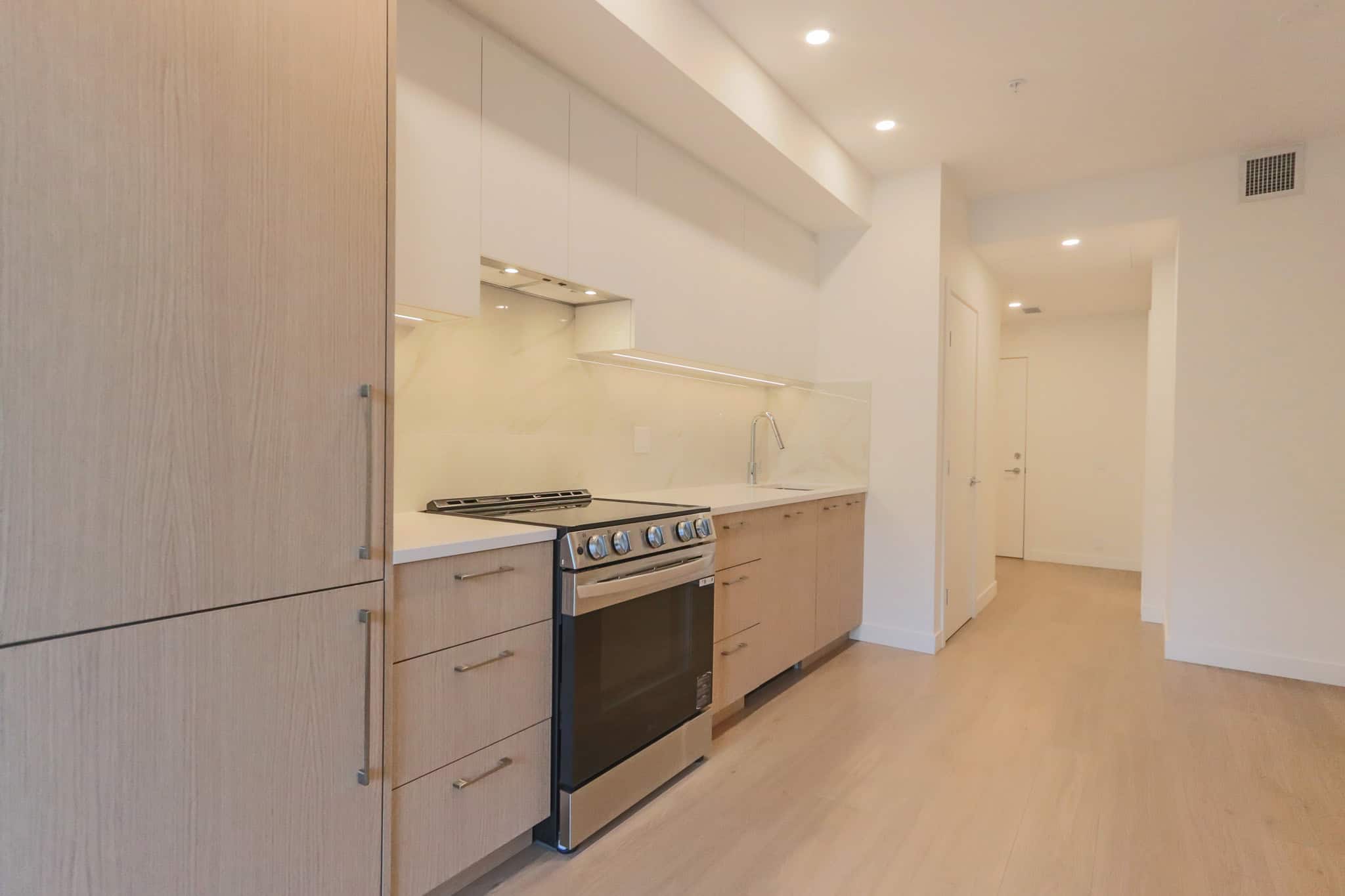 Modern minimalist kitchen with light wood cabinetry, stainless steel appliances, and white countertops in a contemporary Vancouver home.