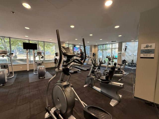 Indoor fitness gym with cardio equipment and large windows, ideal for health-conscious clients at Orca Realty Inc., Vancouver real estate agency.