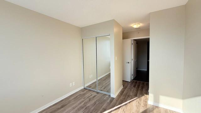 Bright, blank bedroom with mirrored closet doors, neutral walls, hardwood flooring, and an open doorway leading to a hallway, showcasing modern interior space at Orca Realty Inc.