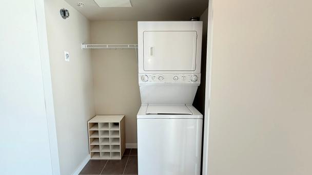 Stacked washer and dryer in a compact laundry space with minimal storage, featuring a small wooden cubby organizer and a wire shelf for convenient laundry room organization.