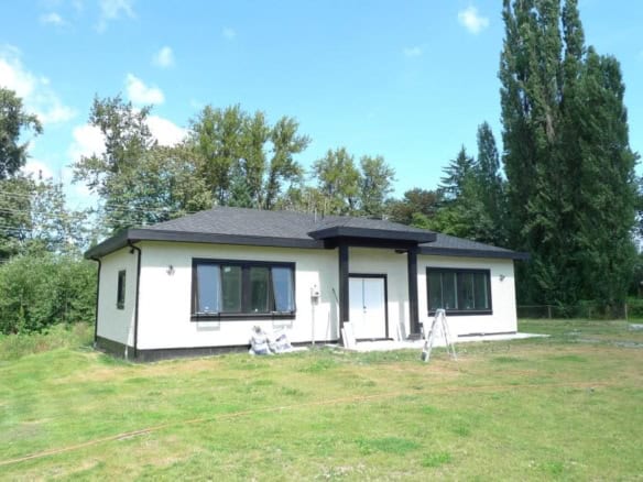 Modern single-family home under construction with black and white exterior, large windows, in a lush green yard, ideal for Vancouver Island real estate investment and family living.