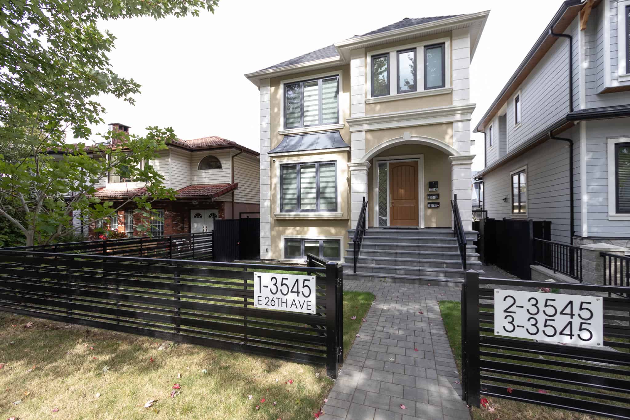 Modern two-storey residential home with elegant exterior, landscaped front yard, and black metal fencing, located in a desirable neighborhood in Vancouver, BC.