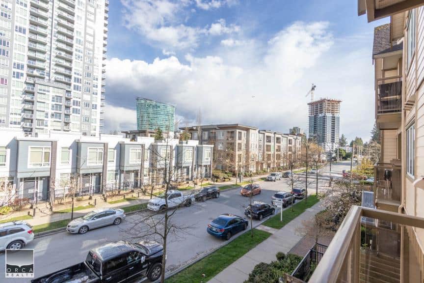 Modern urban residential street with contemporary townhouses and high-rise building in Vancouver, BC, featuring a sunny day and city skyline.