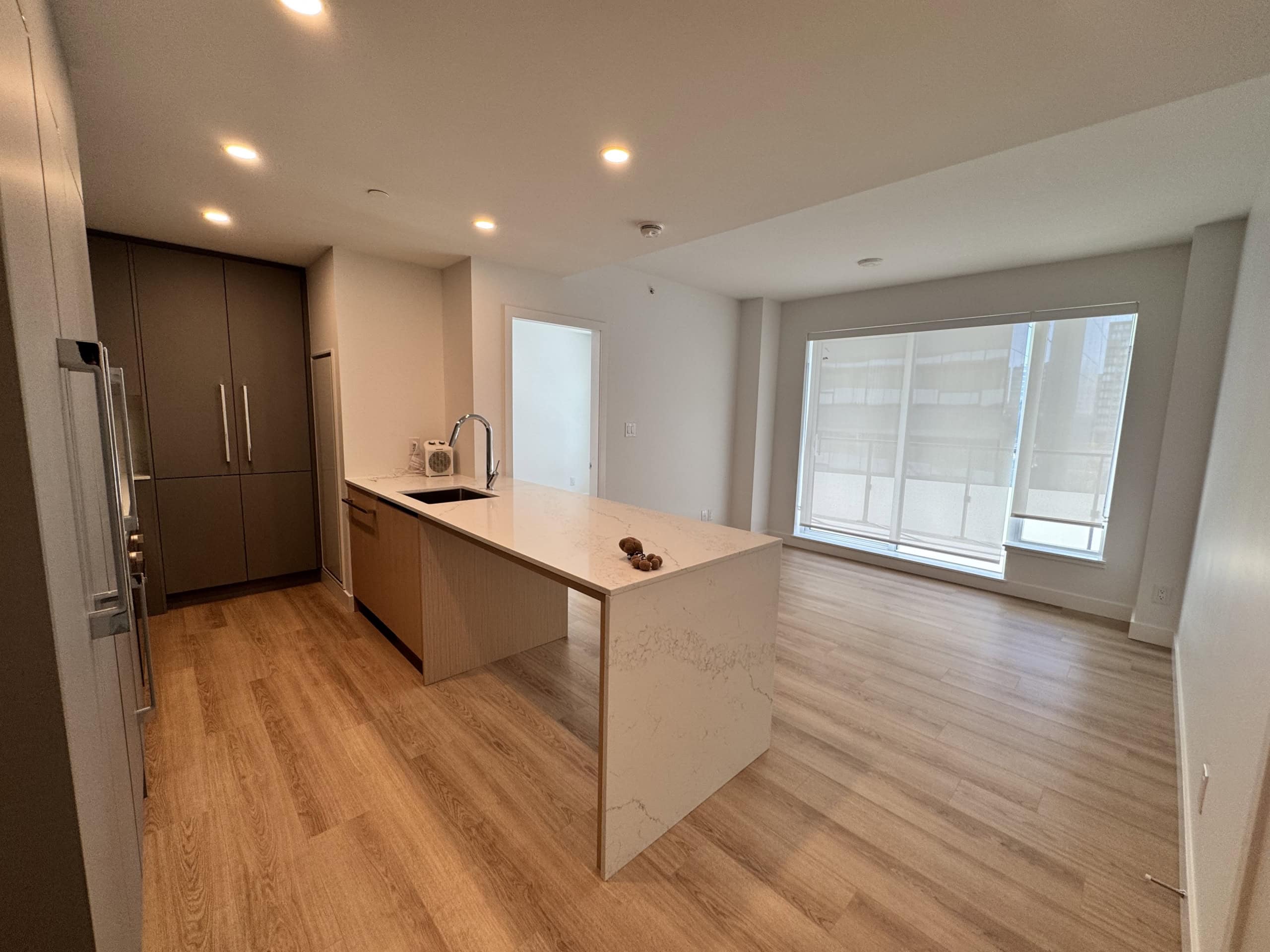 Contemporary open-concept kitchen and living area in a modern Vancouver apartment, featuring natural light, wood flooring, sleek cabinetry, and a spacious layout ideal for urban living.