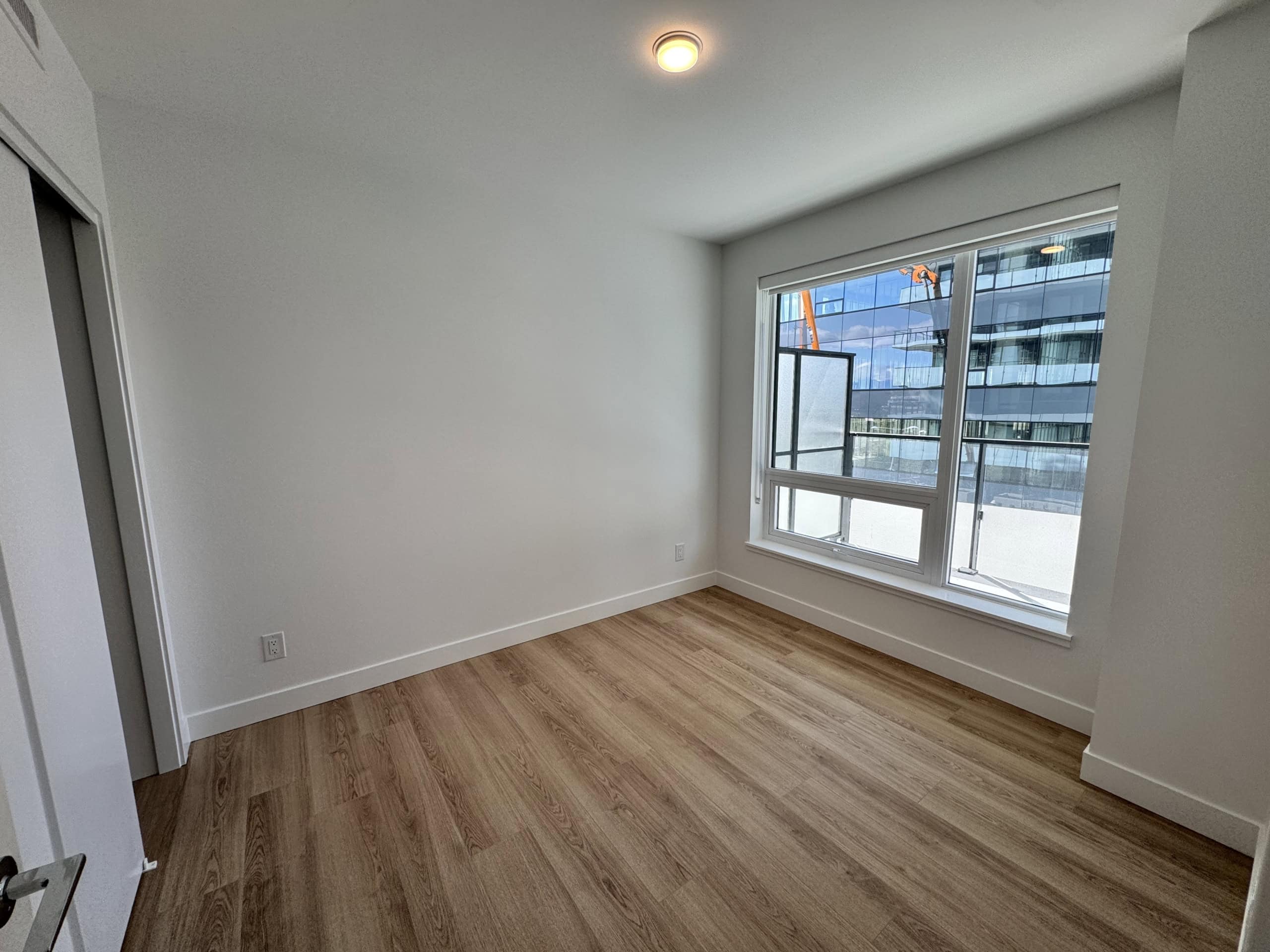 Bright modern bedroom with large window, hardwood flooring, and fresh white walls in a high-rise condo near downtown Vancouver. Perfect for urban living and investment in Vancouver real estate.
