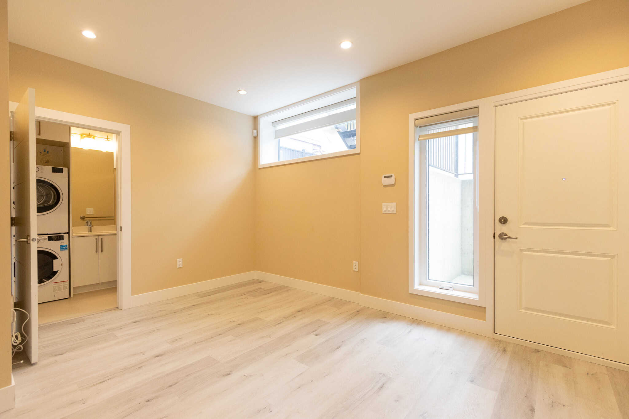 11 Bright modern living room with beige walls, white trim, and light wood flooring. Features a door to a small outdoor area, large window for natural light, and access to laundry room. Perfect for Vancouver homebuyers.