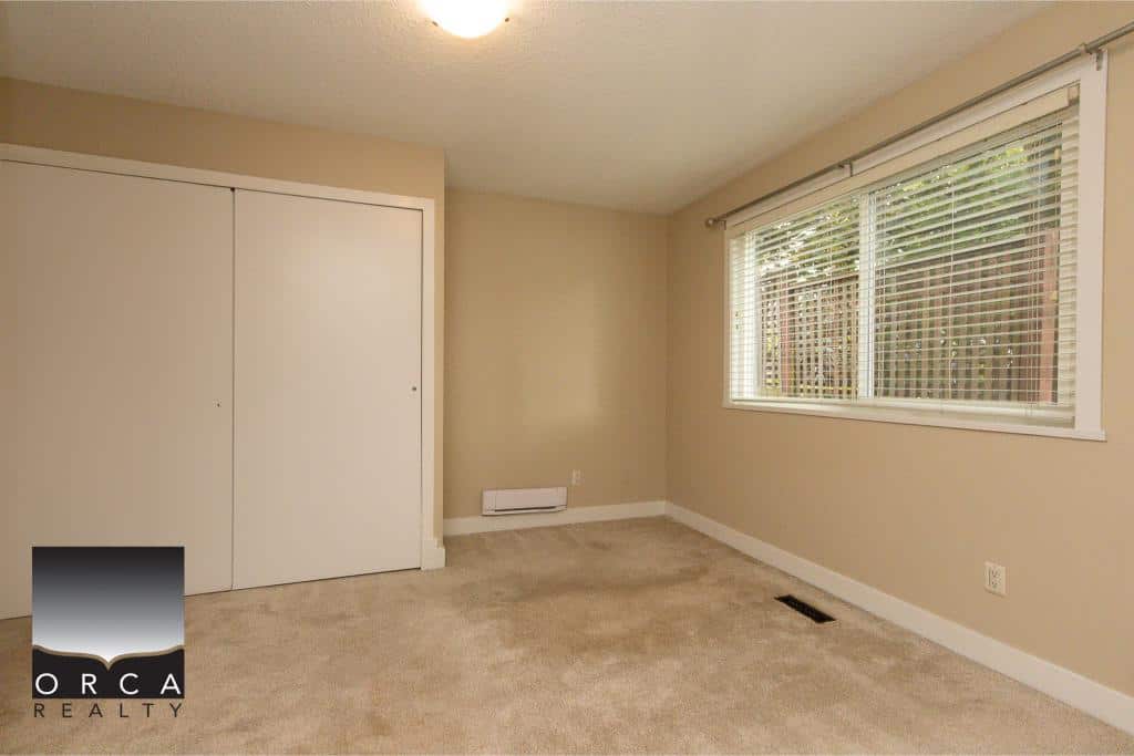 Bright interior room with large window, beige walls, and closet space, ideal for real estate listings showcasing homes in Victoria, BC, by Orca Realty Inc.
