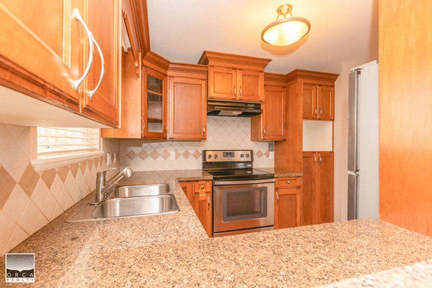 Bright and updated kitchen with wooden cabinetry, stainless steel appliances, granite countertops, and a tiled backsplash, ideal for modern family living and entertaining.