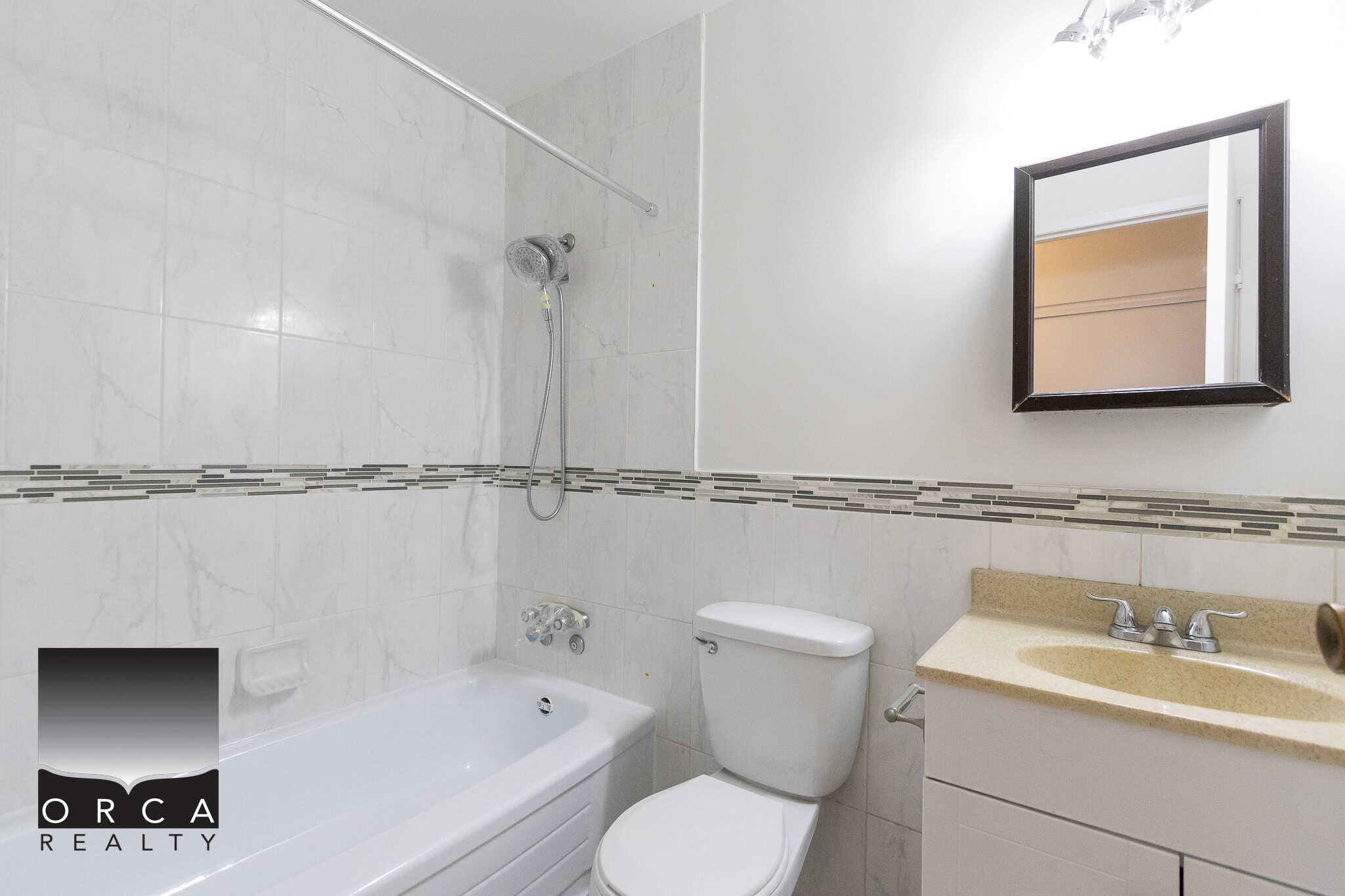 Clean modern bathroom with bathtub, toilet, and beige vanity, featuring neutral tile decor and a wall-mounted mirror. Ideal for Vancouver Island homes and real estate listings.