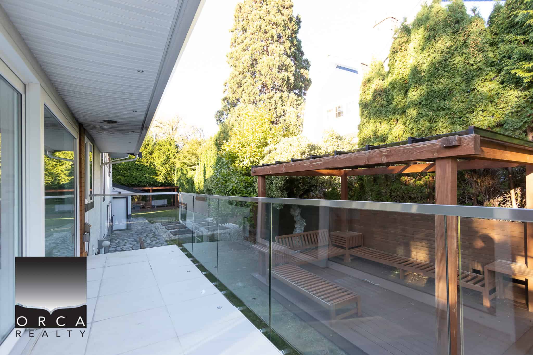 Contemporary balcony with glass railing, overlooking a lush green backyard with mature trees, ideal for Vancouver real estate and outdoor living.