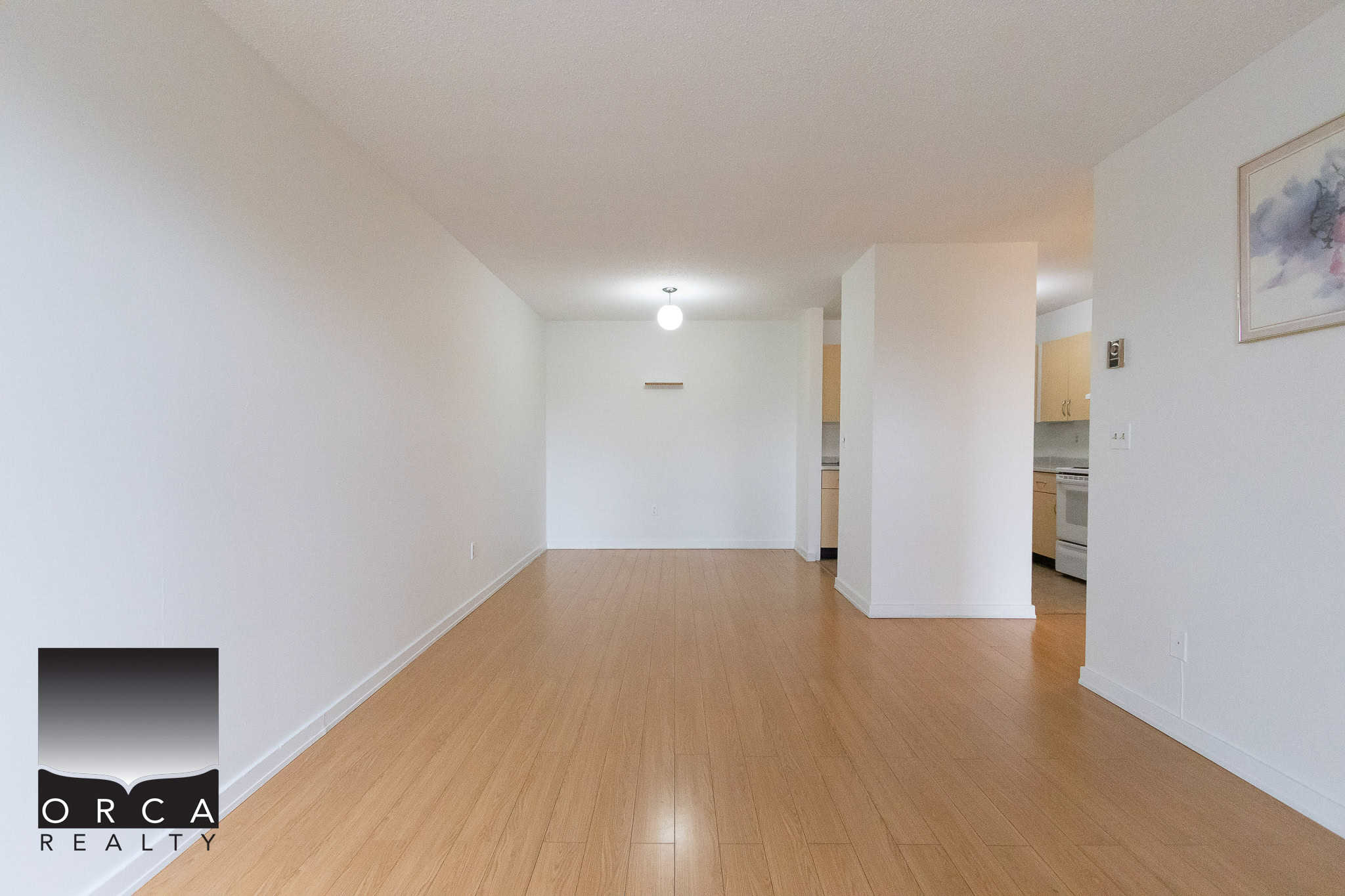 Bright empty living room with white walls and wooden flooring, open concept kitchen in the background, ideal for Vancouver-area home buyers seeking modern condos or apartments.