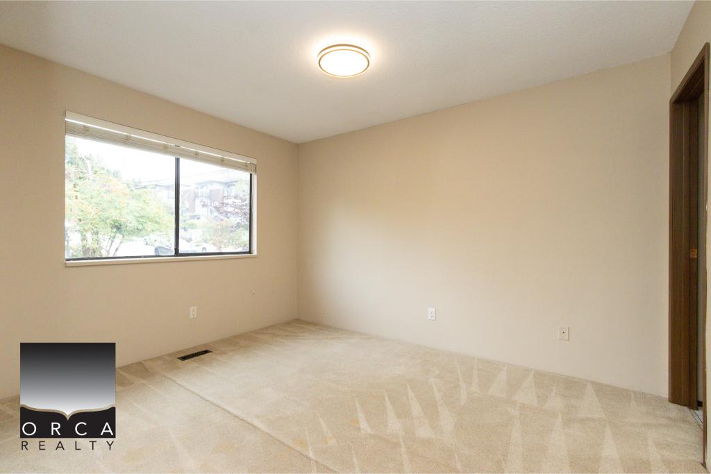 Bright empty bedroom with large window, beige carpet, and neutral walls, ideal for homebuyers seeking a cozy space in a Vancouver property listing.