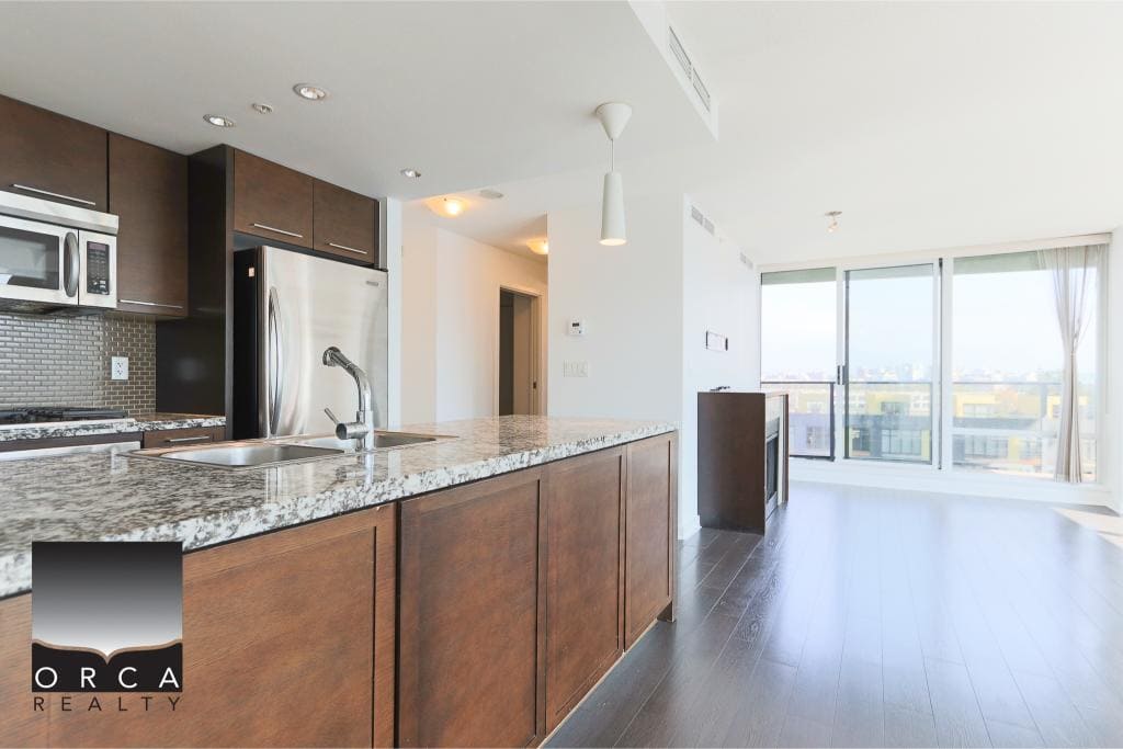 Modern urban condo kitchen with granite countertops, stainless steel appliances, and large windows offering city views, brought to you by Orca Realty Inc.
