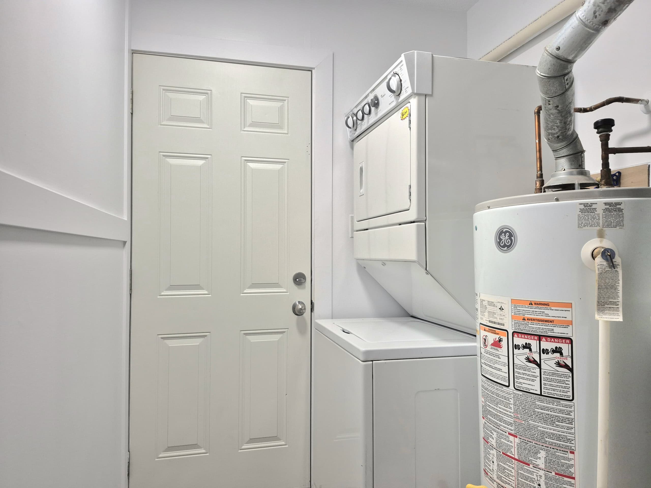 20250920_141433 Clean laundry room with stacked washer and dryer, white walls, and utility water heater, ideal for residential property listings on Orca Realty Inc.