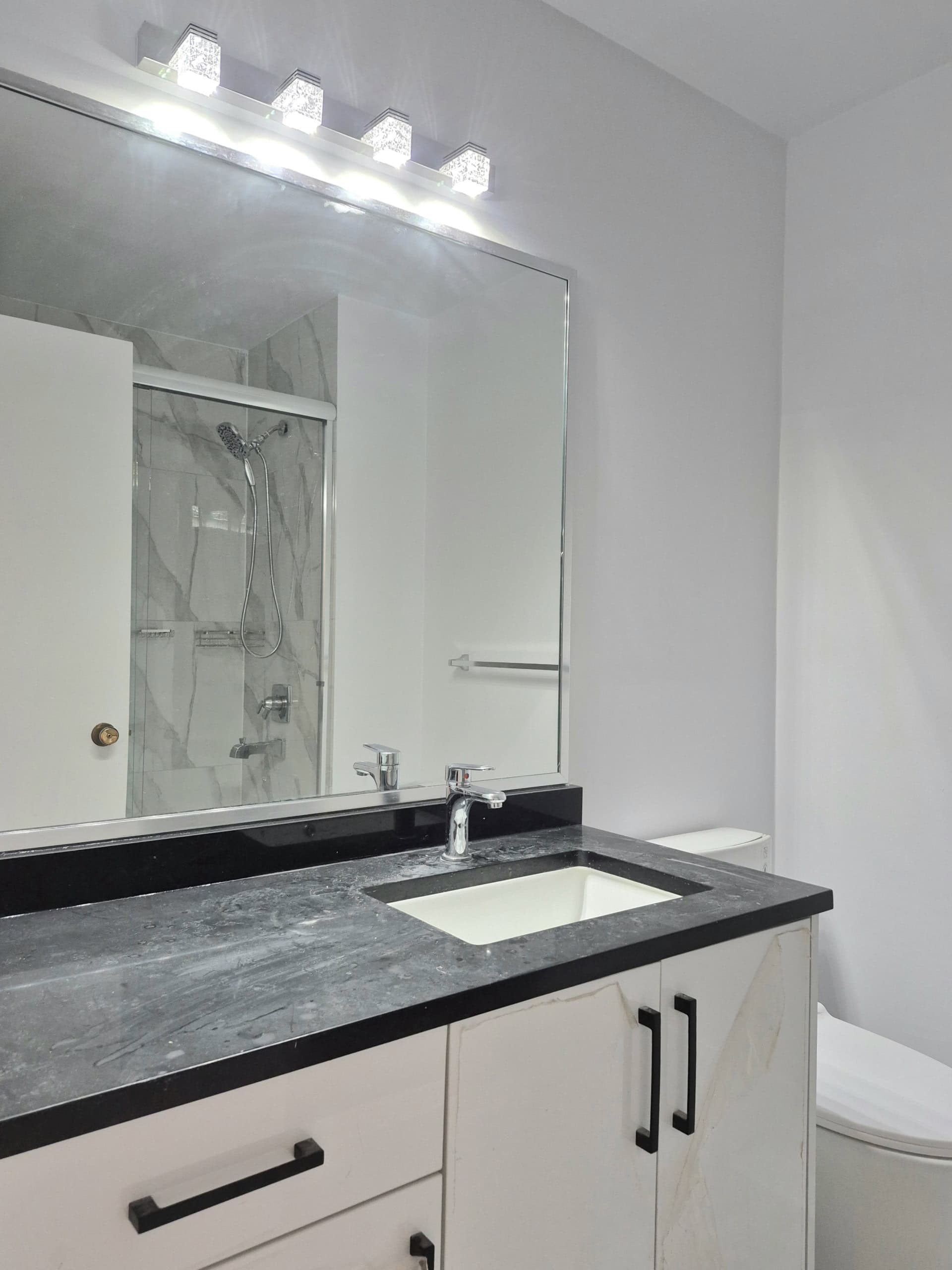 20250920_141454 Modern bathroom with vanity sink, black countertop, and large mirror, featuring elegant cabinetry, sleek black handles, and contemporary lighting, ideal for upscale real estate in Ottawa.
