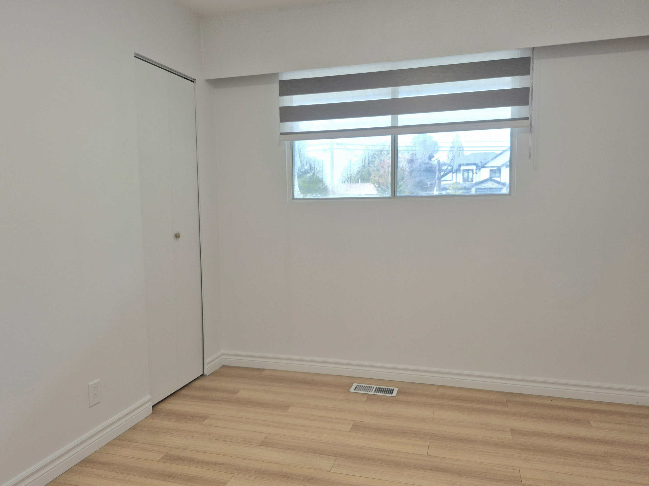 20250920_141610 Bright empty bedroom with white walls, wooden flooring, a single window with modern blinds, and a closet door, showcasing a clean and minimalistic space available for Vancouver real estate listings.