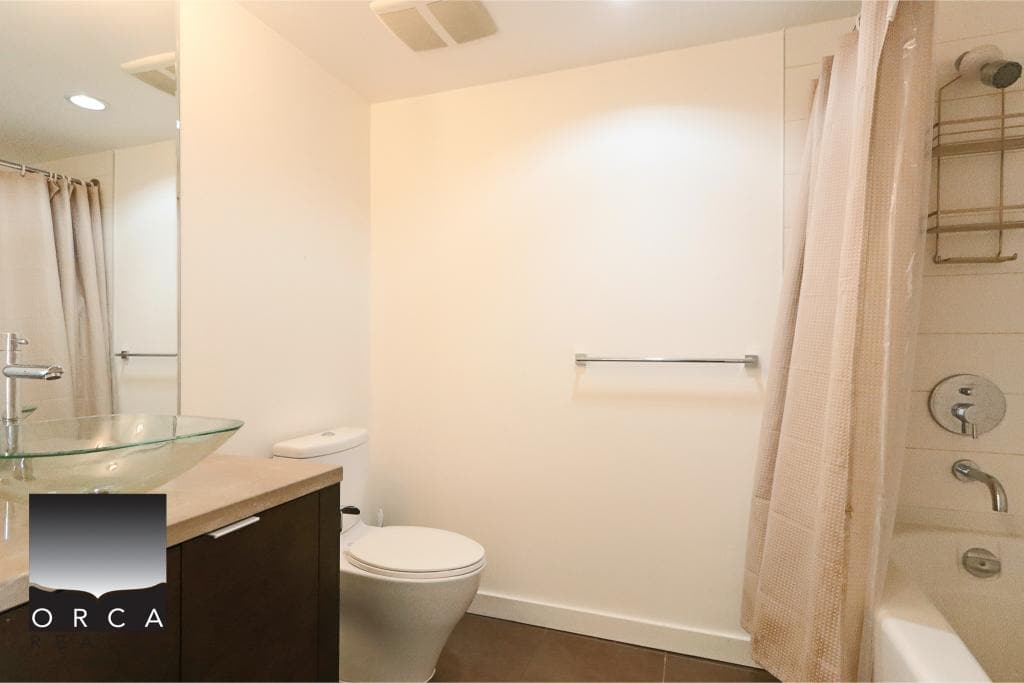 Modern bathroom with glass vessel sink, white toilet, and shower/tub combo with curtain, neutral color scheme, and contemporary fixtures in a property listed by Orca Realty Inc.