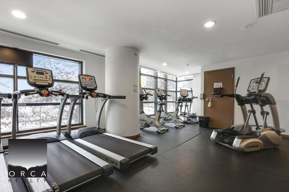 Treadmills and elliptical machines inside a modern gym at Orca Realty Inc. property for fitness and health in a bright, well-equipped space with large windows.