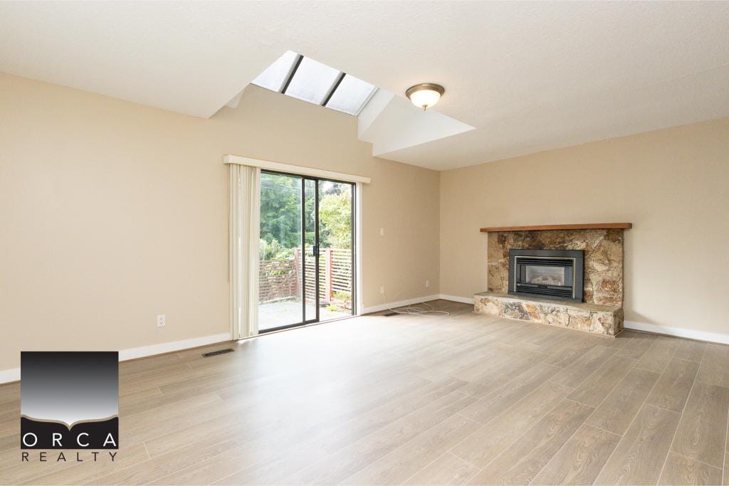 Bright living room with vaulted ceiling, skylight, and sliding glass door leading to outdoor space, featuring a cozy stone fireplace, perfect for Vancouver Island homes.