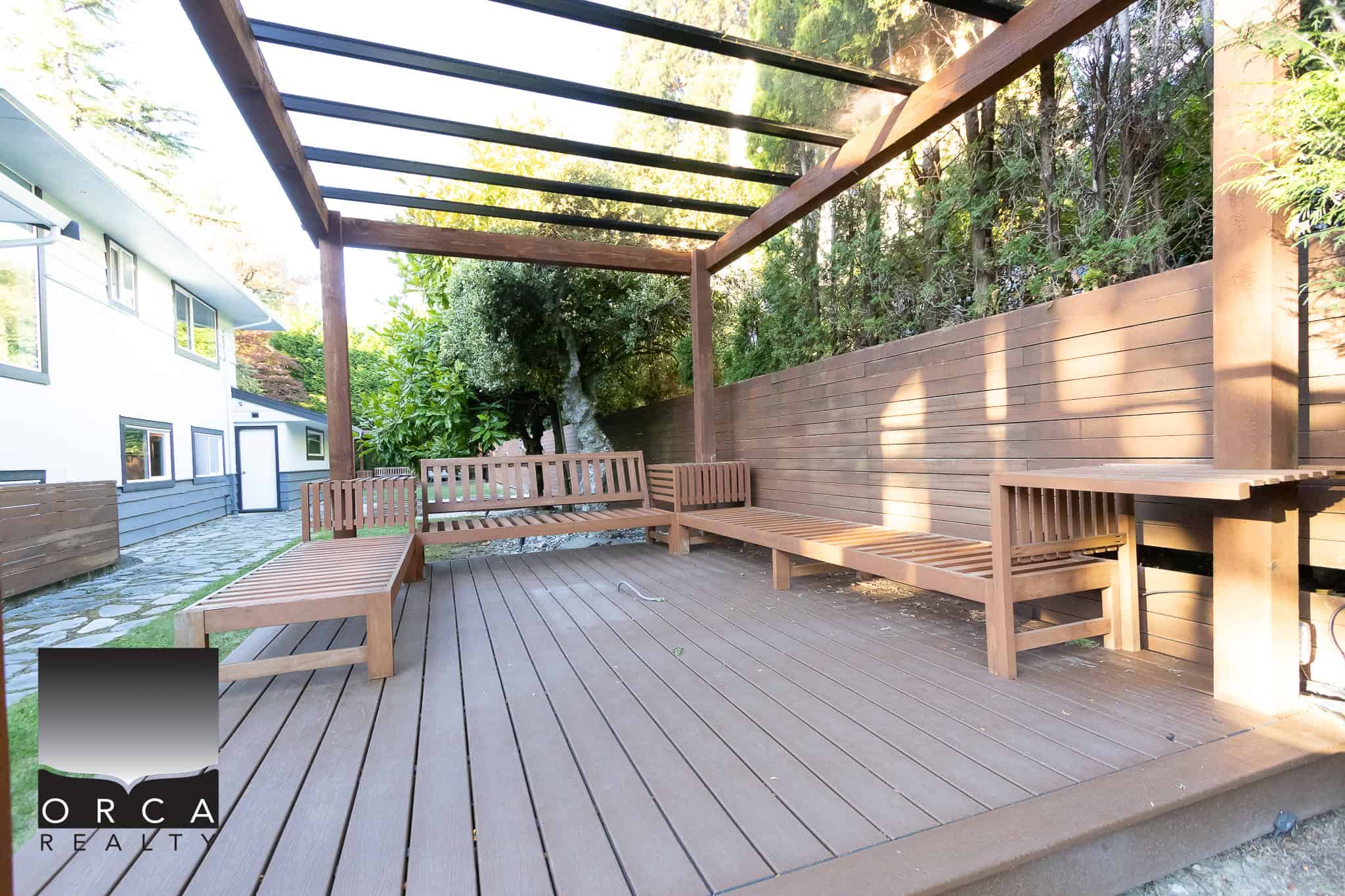 Modern backyard patio with wooden benches and pergola, surrounded by lush greenery and privacy fence, ideal for relaxation and outdoor gatherings in Victoria, BC.