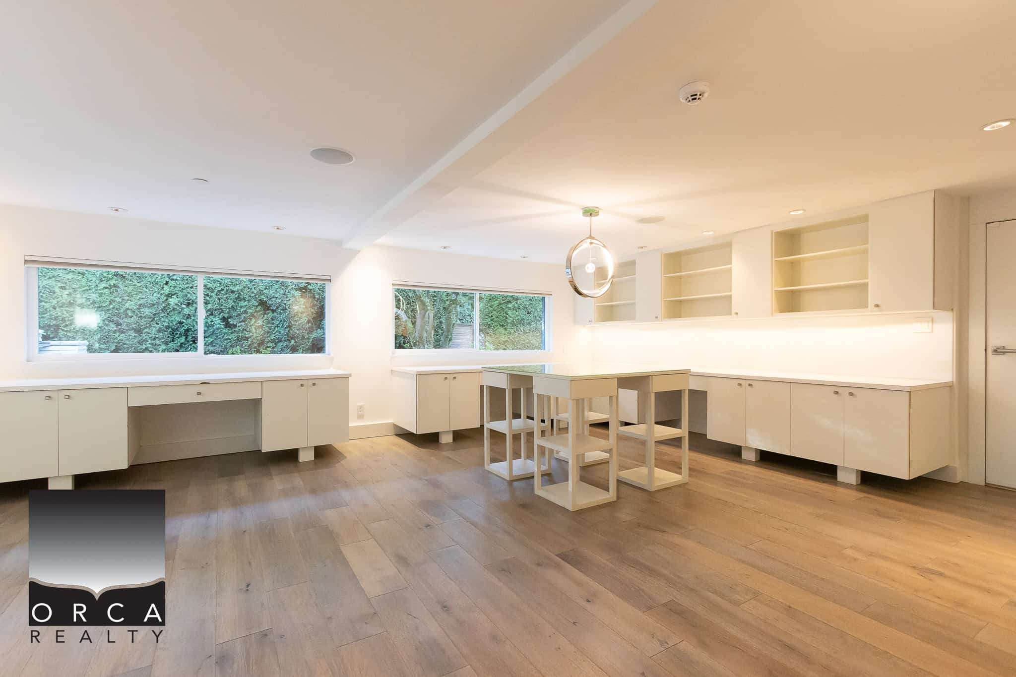 Spacious modern kitchen with white cabinetry, large windows overlooking greenery, and minimalist design, perfect for Vancouver Island real estate listings.