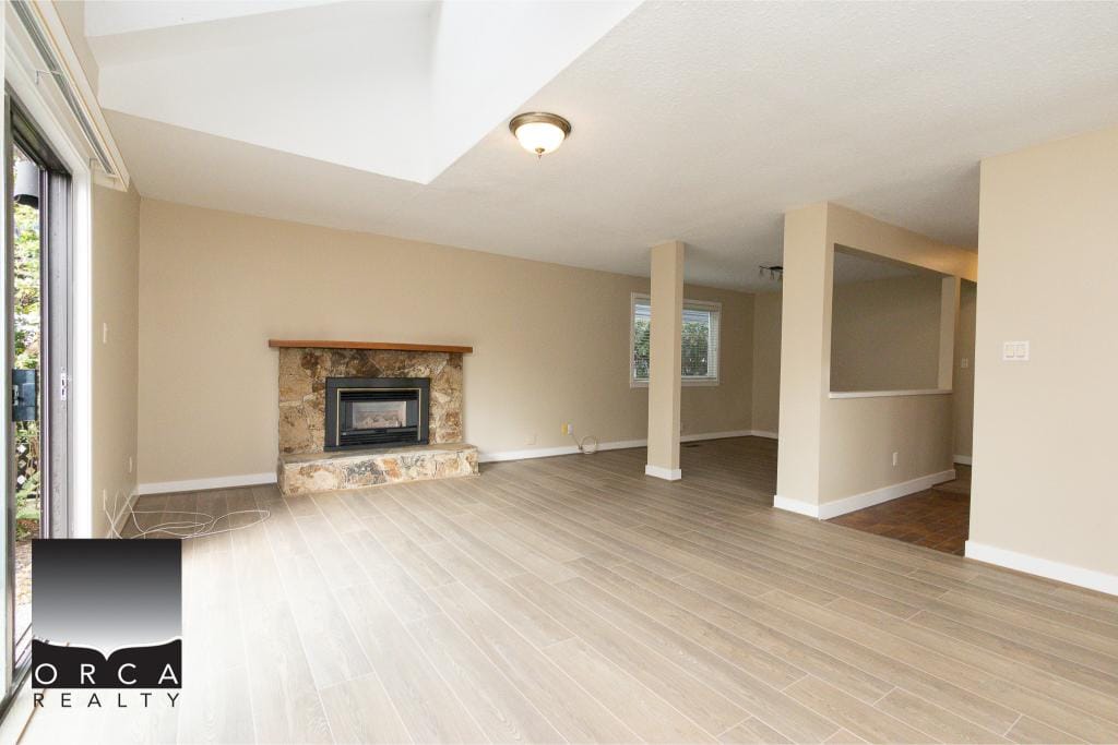 Newly renovated living room with modern wood flooring, stone fireplace, and large windows allowing natural light, perfect for BC home seekers from Orca Realty Inc.