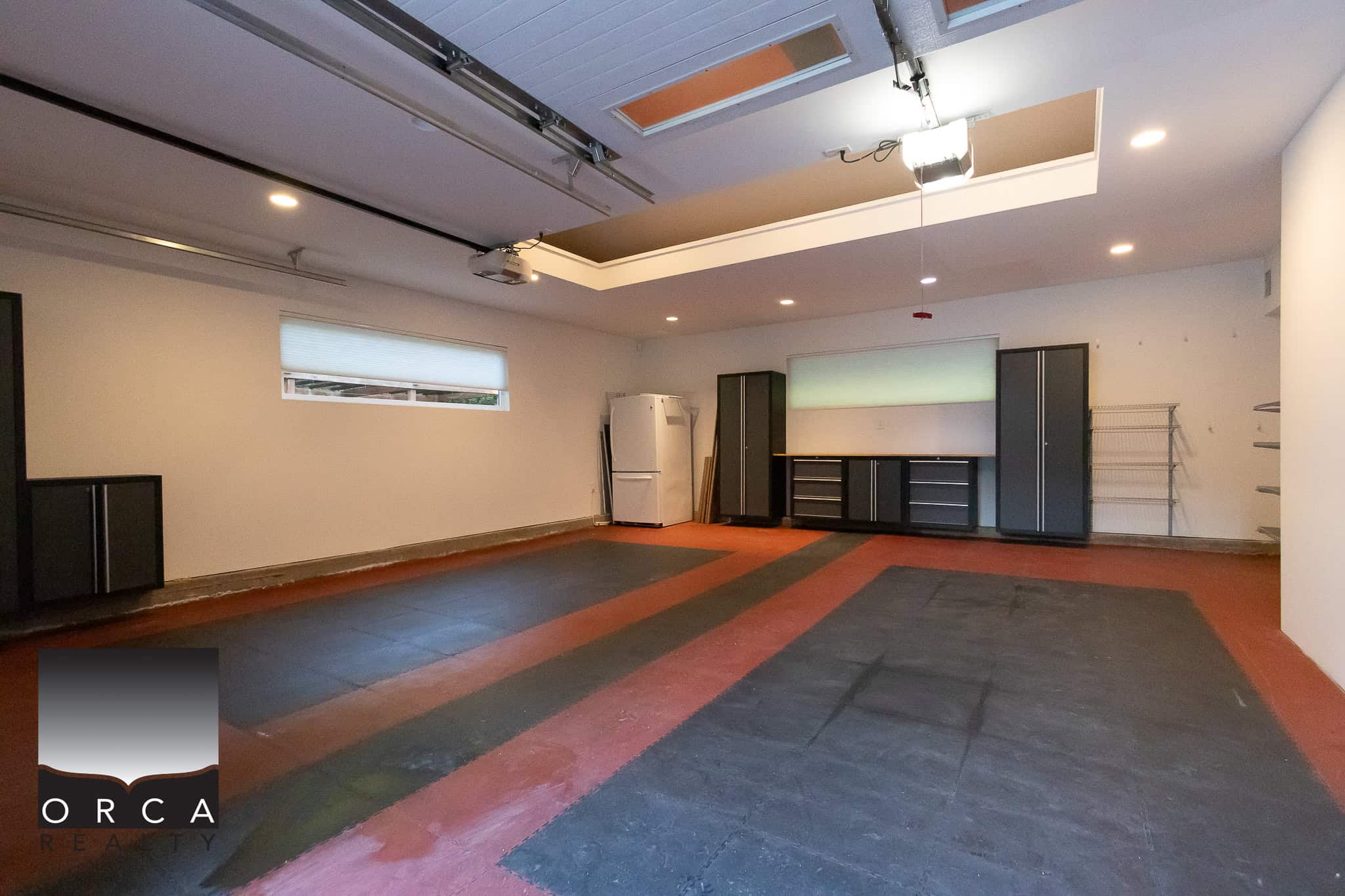 Spacious garage interior with custom storage cabinets, concrete flooring with red and black epoxy coating, and bright lighting, perfect for home organization and vehicle parking.