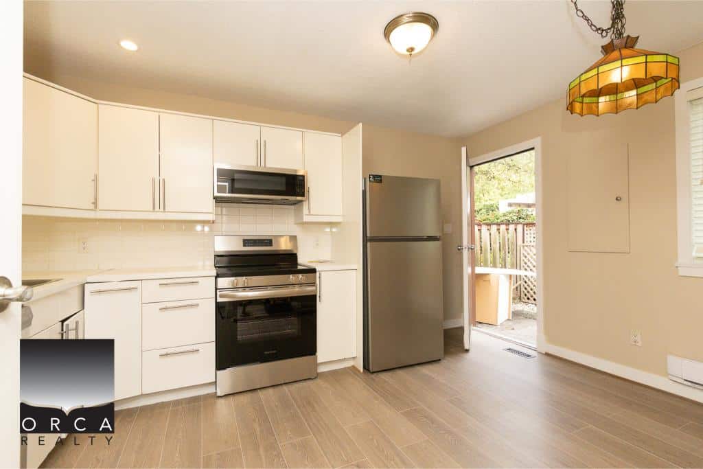 Modern kitchen with stainless steel appliances and white cabinetry in a Vancouver-area home for sale by Orca Realty Inc.