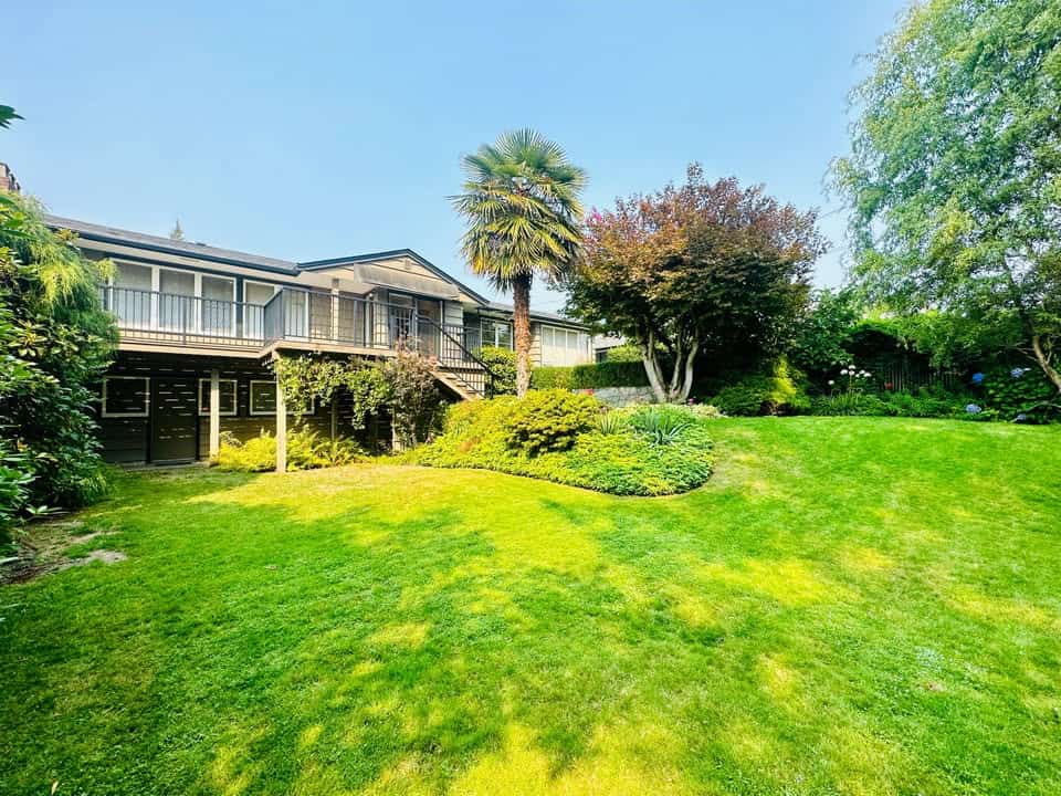 Lush backyard with vibrant green grass, diverse trees, and landscaped garden offers outdoor space for relaxation and entertaining. The property features a raised deck and scenic views, perfect for real estate in BC.