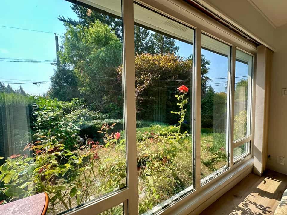 Vivid garden view through large glass sliding door in a modern home, showcasing lush greenery and blooming flowers, ideal for real estate property listings and home exposure on Orca Realty Inc. website.
