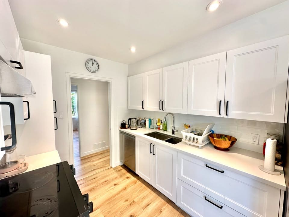 Modern white kitchen with stainless steel appliances and black hardware, featuring ample countertop space, bright lighting, and a cozy, inviting design for Vancouver homebuyers.
