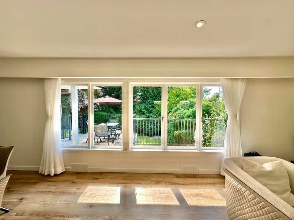 Bright living room with large windows overlooking a lush outdoor patio and garden, ideal for real estate listings and showcasing homes in Vancouver Island.
