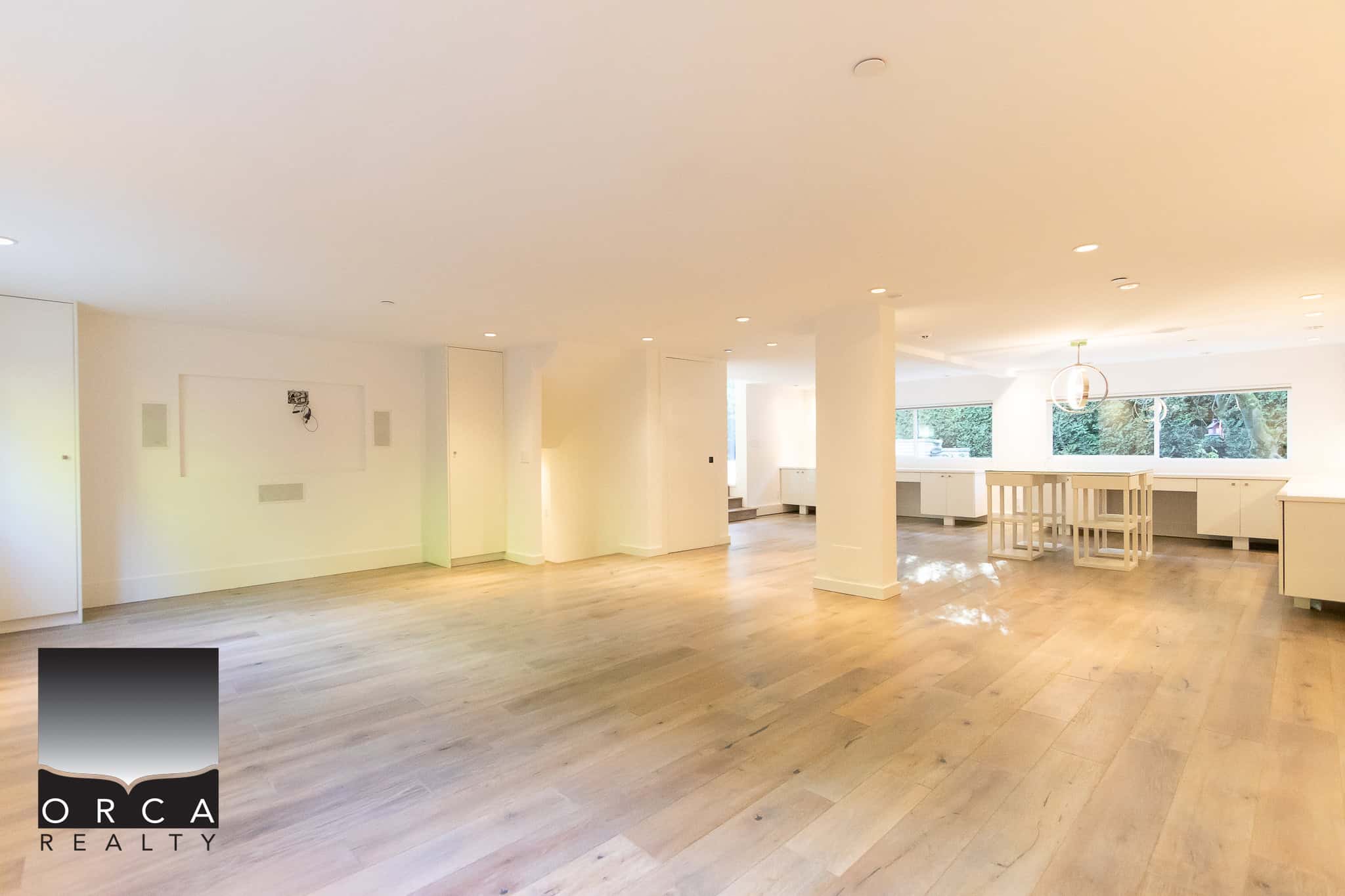 Spacious modern interior of a real estate listing by Orca Realty Inc., showcasing a bright open-concept living area with hardwood floors and large windows.