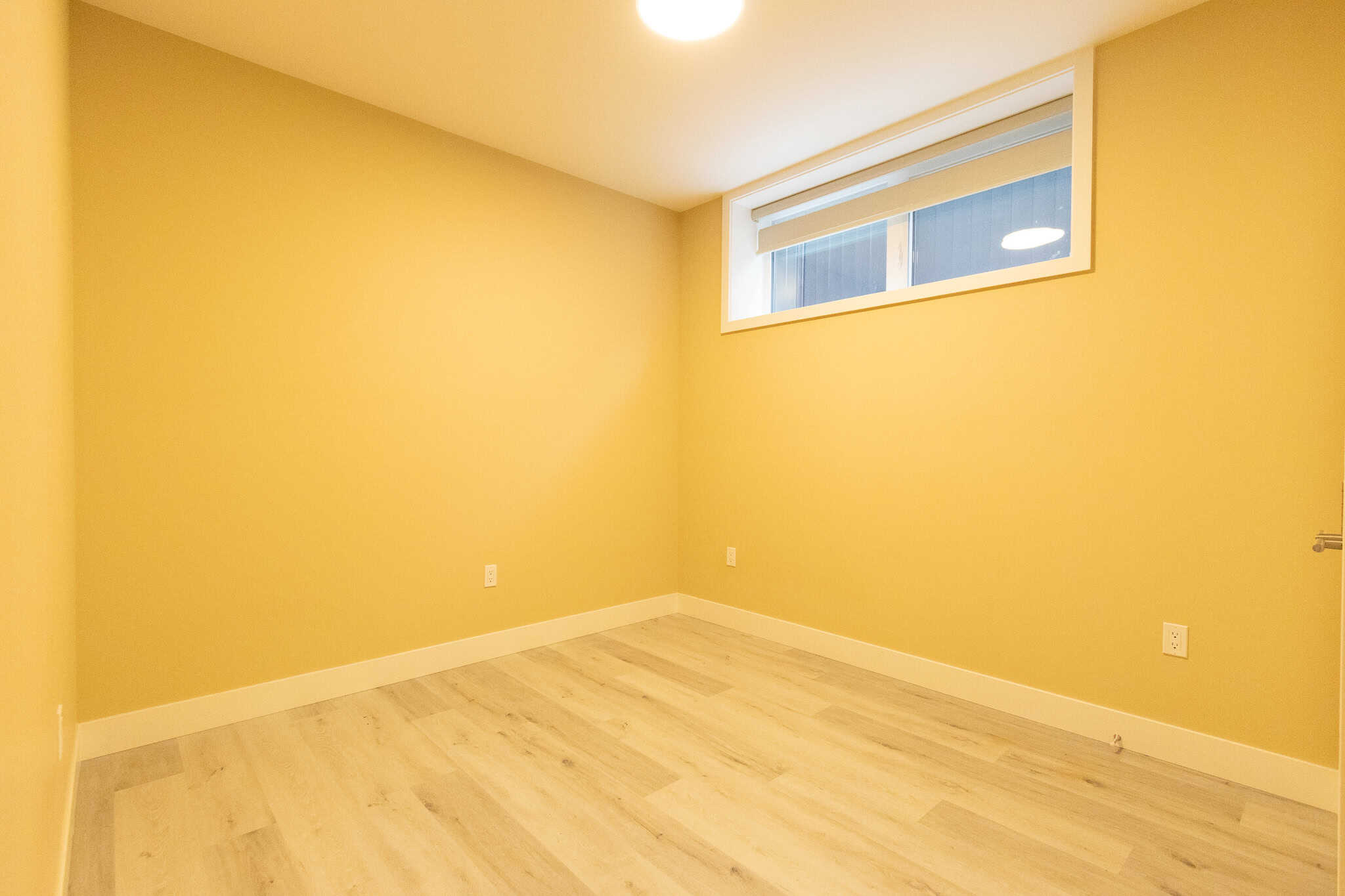 7 Bright yellow-painted neutral room with laminate flooring and a high horizontal window, ideal for modern living or bedroom in properties listed by Orca Realty Inc.