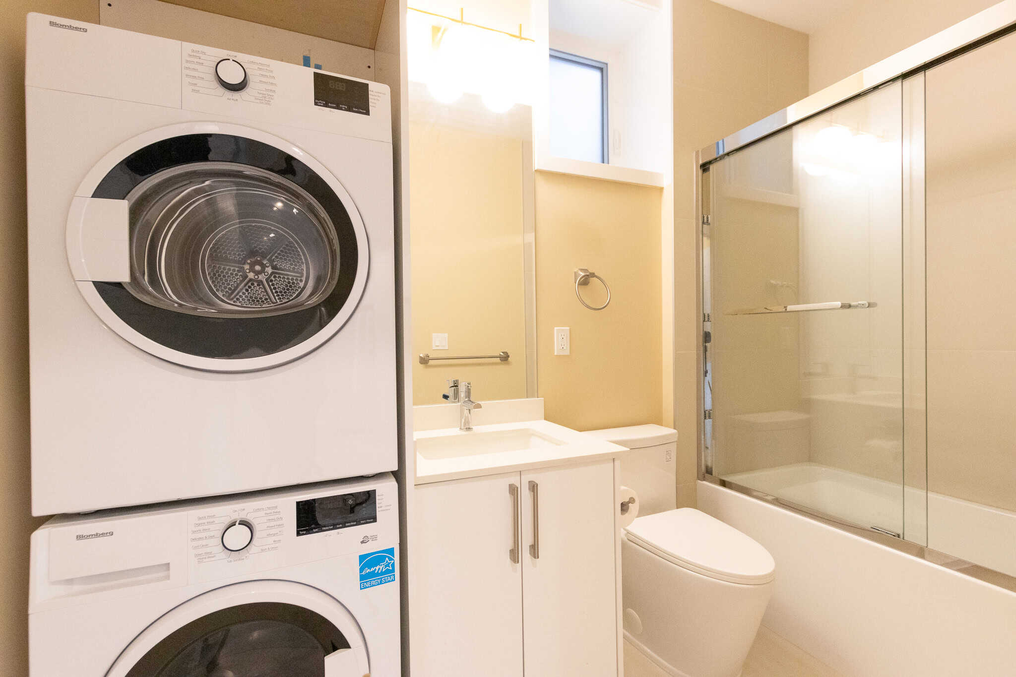 8 Modern laundry room with stacked washer and dryer, sleek vanity with mirror, and spacious glass-enclosed shower, ideal for Vancouver homebuyers searching for stylish, functional bathroom and laundry areas.