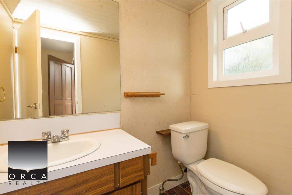 Bright bathroom interior with a white toilet and sink, small window, minimal decor, wooden accents, and neutral-colored walls, showcasing a cozy and functional space in Vancouver real estate listings.