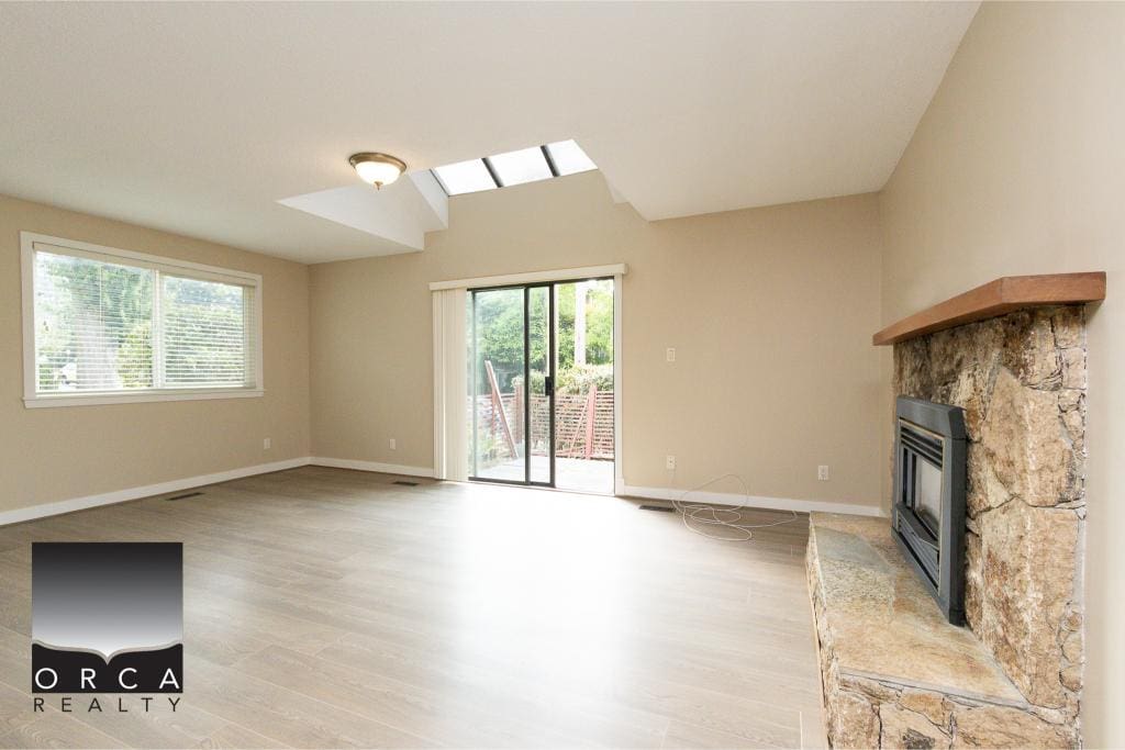 Bright living room with large windows, sliding glass door to patio, natural light, vaulted ceiling with skylight, and cozy stone fireplace, ideal for Vancouver real estate and homebuyers.