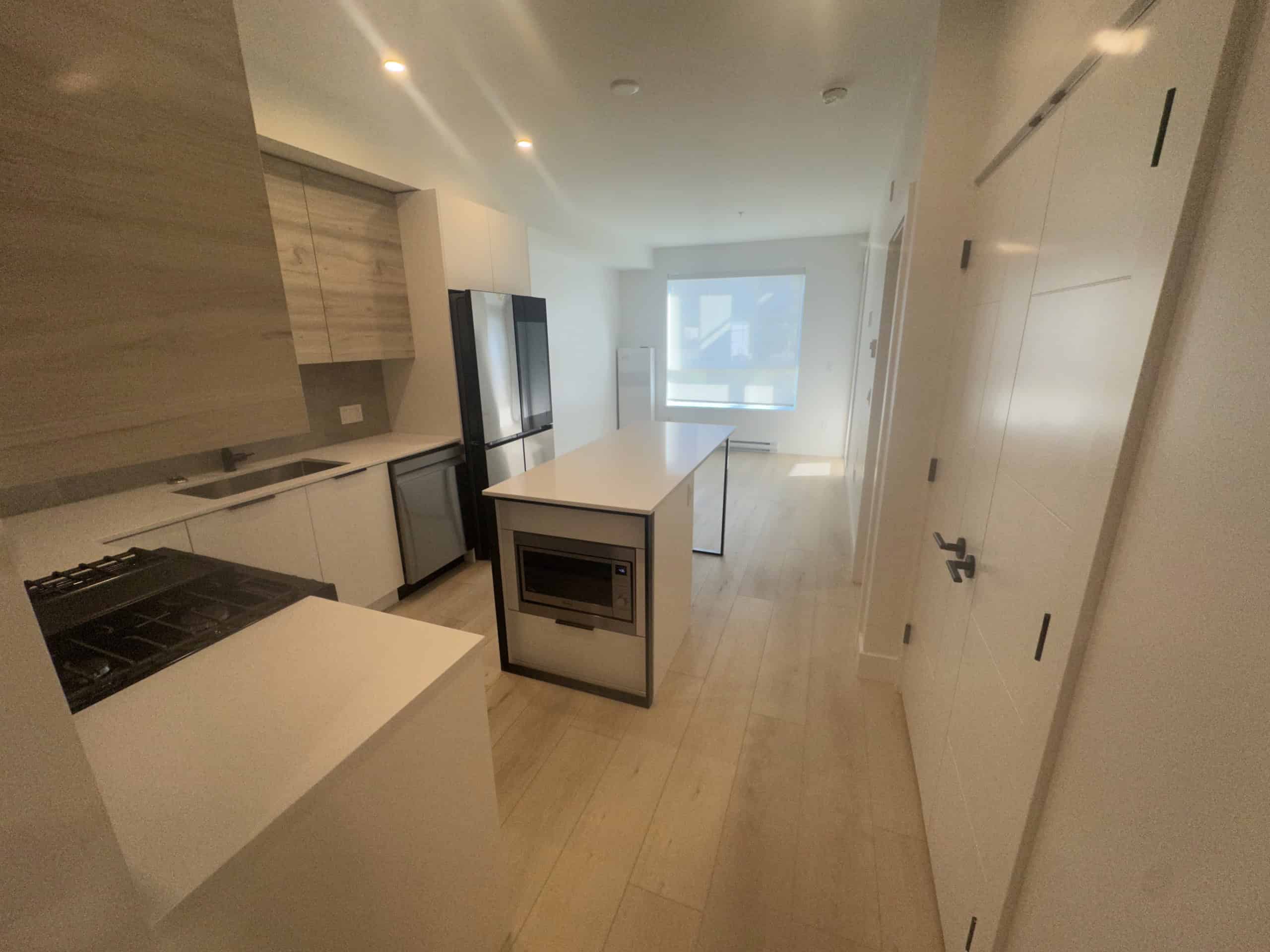 Modern minimalist kitchen interior with white cabinetry and stainless steel appliances, bright natural light from large window, ideal for Vancouver real estate listings.