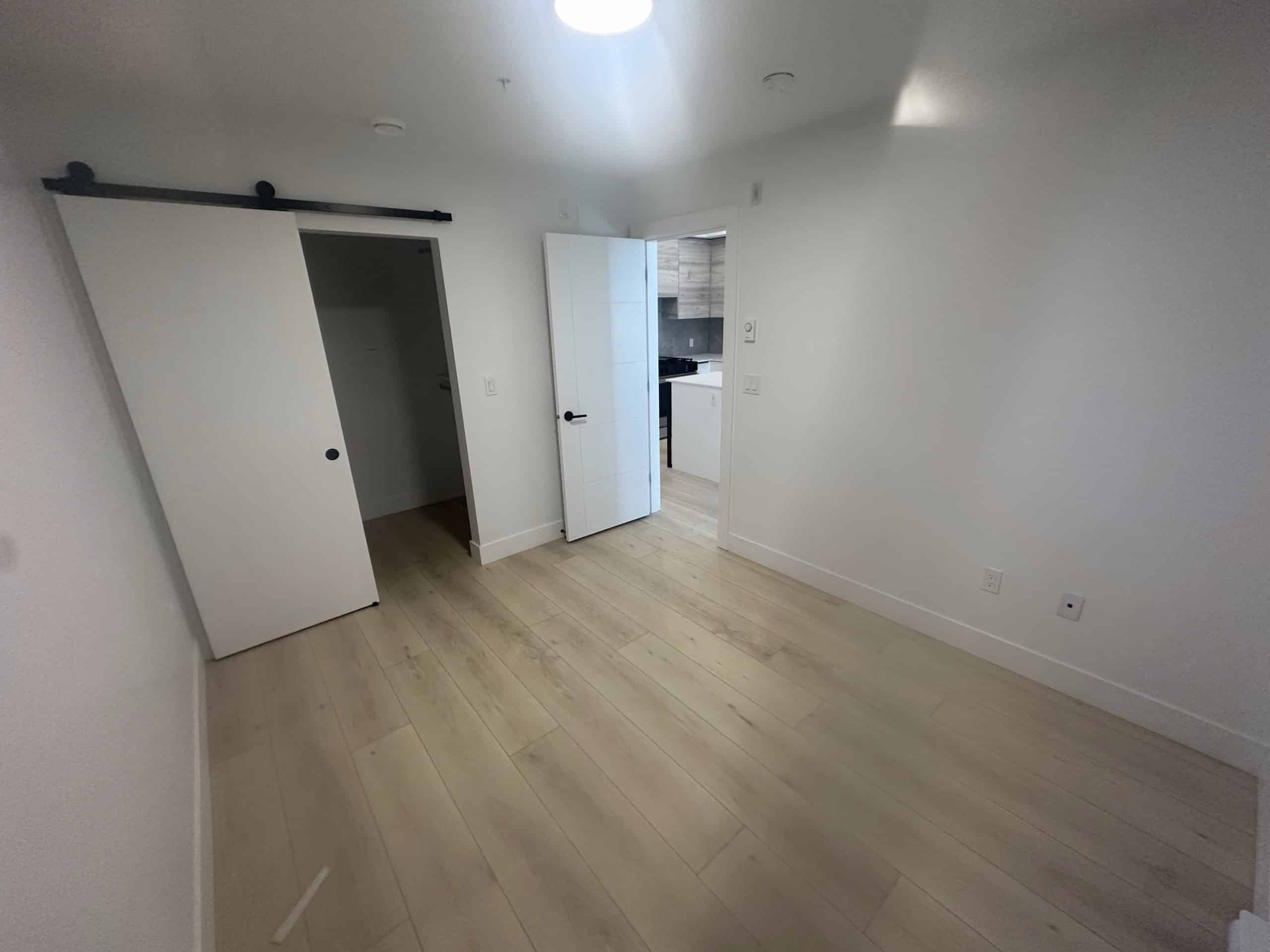 Bright modern vacant bedroom with white walls, light wood flooring, sliding door closet, open door to kitchen, showcasing sophisticated real estate listing in Toronto.
