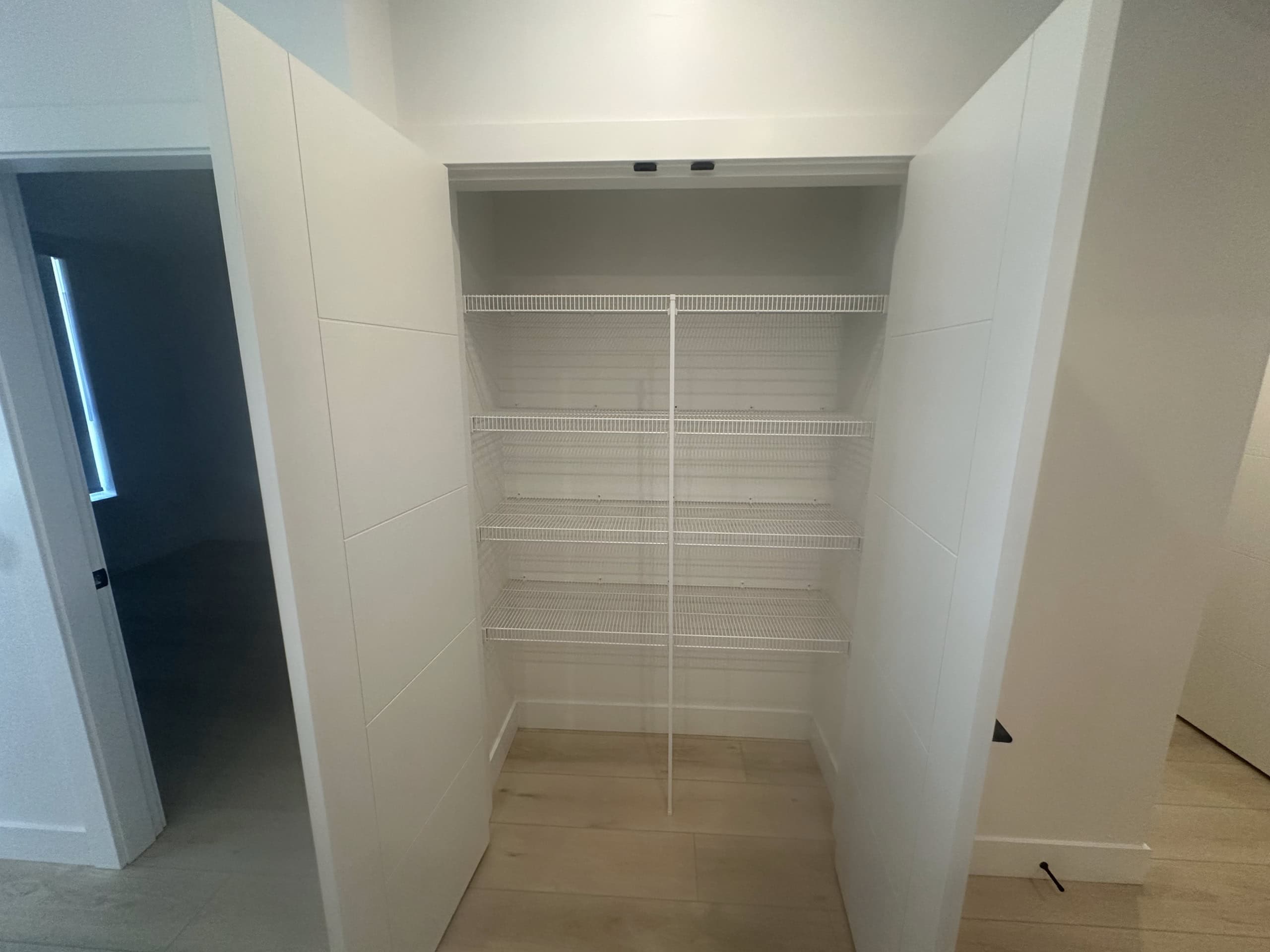 Spacious walk-in pantry with white wire shelves, ideal for organized storage in a modern home.